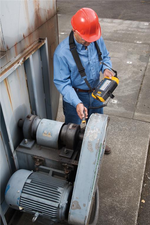 A maintenance technician uses a handheld Fluke 810 Vibration Tester on a belt-driven fan setup.