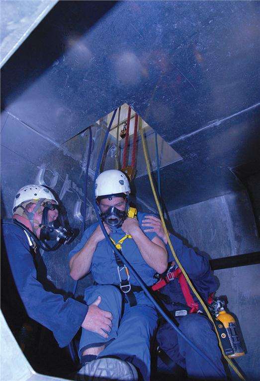Two rescuers have located the victim and pulled him to a spot beneath the roof hatch. While attaching the haul system to his harness, they must also keep their own air hoses and lifelines from tangling. So far, the rescue has taken about 20 minutes. The tasks are realistic, completely absorbing and quite strenuous. Photo: Carroll McCormick
